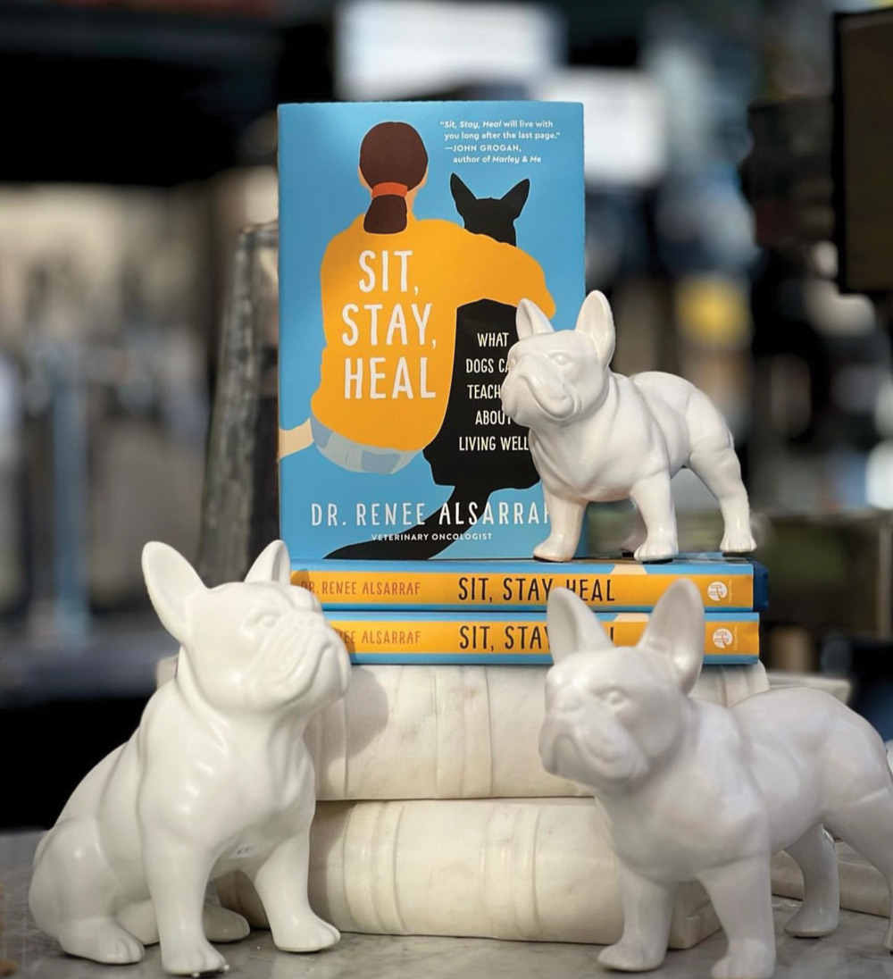 small stack of Sit, Stay, Heal books surrounded by ceramic french bulldog dog statues